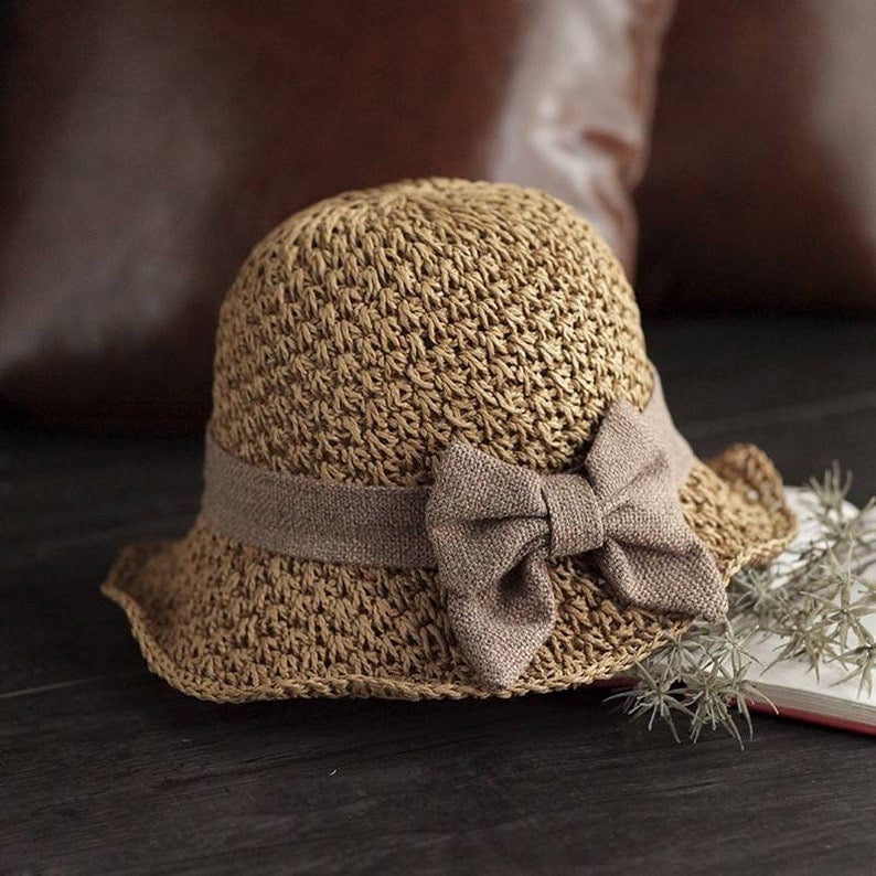 Fransk stil med rosett 👒 — Andningsbar vävd design, bred vågig brätte, solskydd och ansiktsminskande effekt. Justerbar passform (blåser inte bort!), vikbar och packbar 🌊